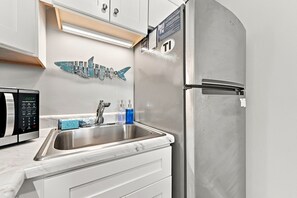 Eine Küche mit einem Edelstahl-Kühlschrank, einer Mikrowelle und einem Waschbecken mit Marmorarbeitsplatte.