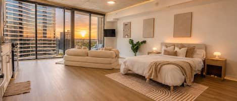 A modern bedroom with a large bed, a sofa, and a view of a cityscape through large windows.