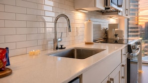 Una cocina moderna con un lavamanos de acero inoxidable, azulejos blancos tipo metro y vistas de la ciudad a través del ventanal.