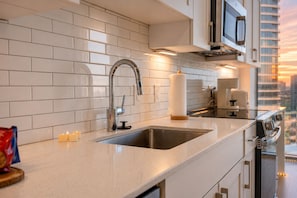A modern kitchen with a stainless steel sink, white subway tiles, and a view of the cityscape through the window. - Cozy Lux Studio with Rooftop Pool and Balcony Overlooking the City  (Atlanta)