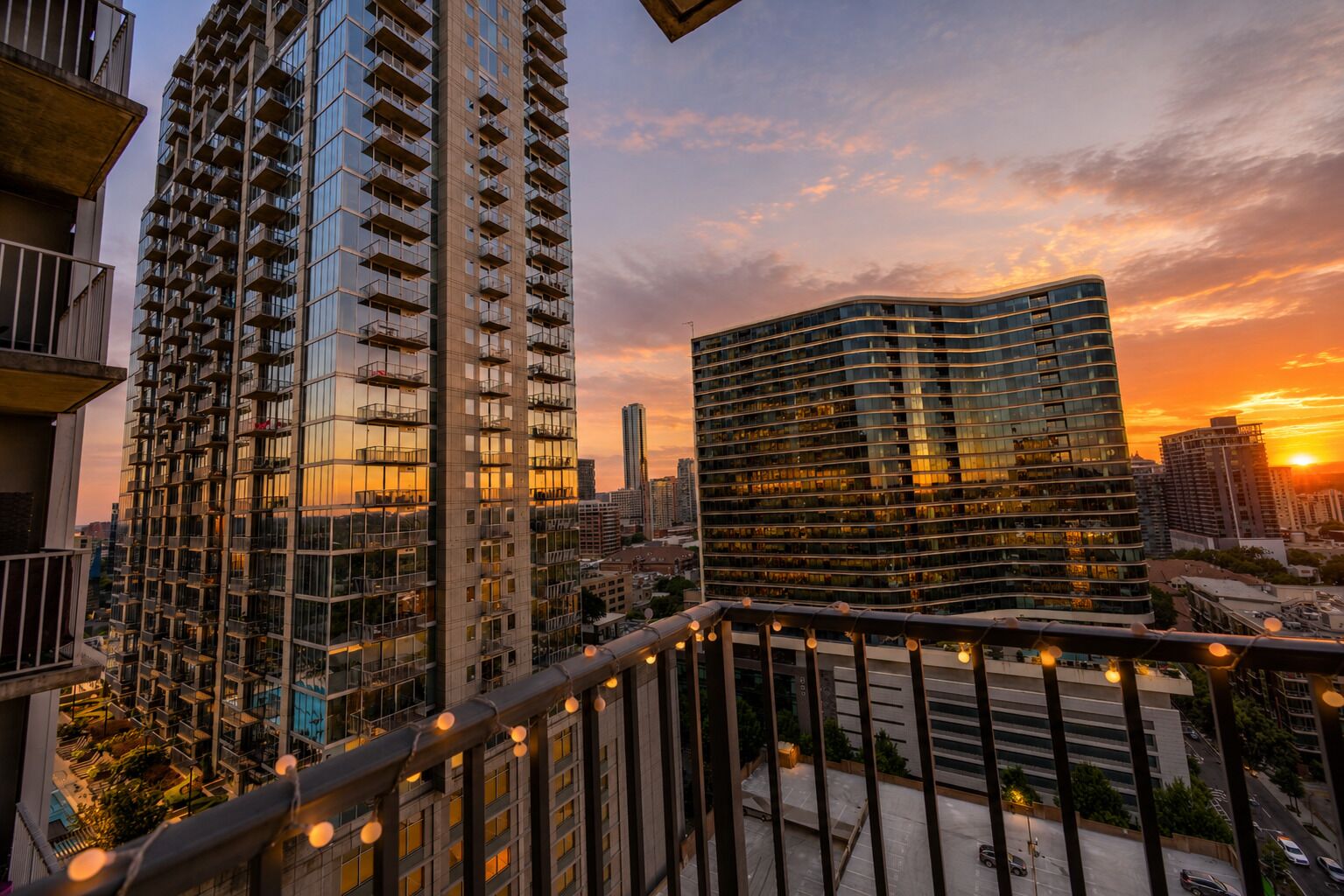 A high-rise building with multiple balconies and a curved glass facade, set against a sunset sky.