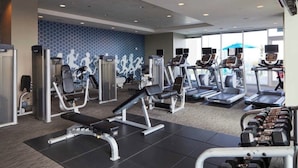 Un gimnasio con varios equipos de ejercicio, incluyendo cintas de correr y máquinas de pesas, y una pared estampada al fondo.