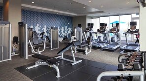 A gym with various exercise equipment, including treadmills and weight machines, and a patterned wall in the background. - Cozy Lux Studio with Rooftop Pool and Balcony Overlooking the City  (Atlanta)