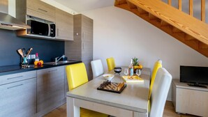 A modern kitchen with a microwave, sink, and wooden cabinets. There is a dining table with yellow chairs and a TV in the corner. - Seaside Apartment in Biscarrosse (Biscarrosse)