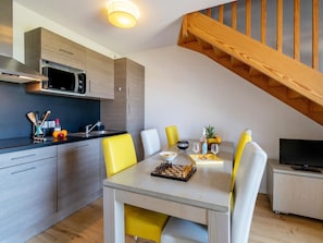 A modern kitchen with a microwave, sink, and wooden cabinets. There is a dining table with yellow chairs and a TV in the corner. - Seaside Apartment in Biscarrosse (Biscarrosse)