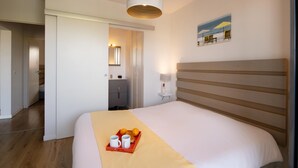 A hotel room with a bed, a bedside table with a lamp, a tray with oranges and mugs, and a painting on the wall. - Seaside Apartment in Biscarrosse (Biscarrosse)