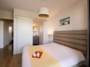 A hotel room with a bed, a bedside table with a lamp, a tray with oranges and mugs, and a painting on the wall. - Seaside Apartment in Biscarrosse (Biscarrosse)