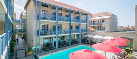 A multi-story hotel with a swimming pool, outdoor seating, and a view of the surrounding area.