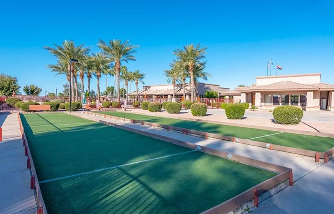 A hotel with a green artificial turf area, palm trees, and a building with a flat roof.