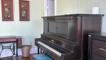 A room with a grand piano, a wooden desk, a wicker basket, and a patterned rug.