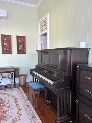 A room with a grand piano, a wooden desk, a wicker basket, and a patterned rug.