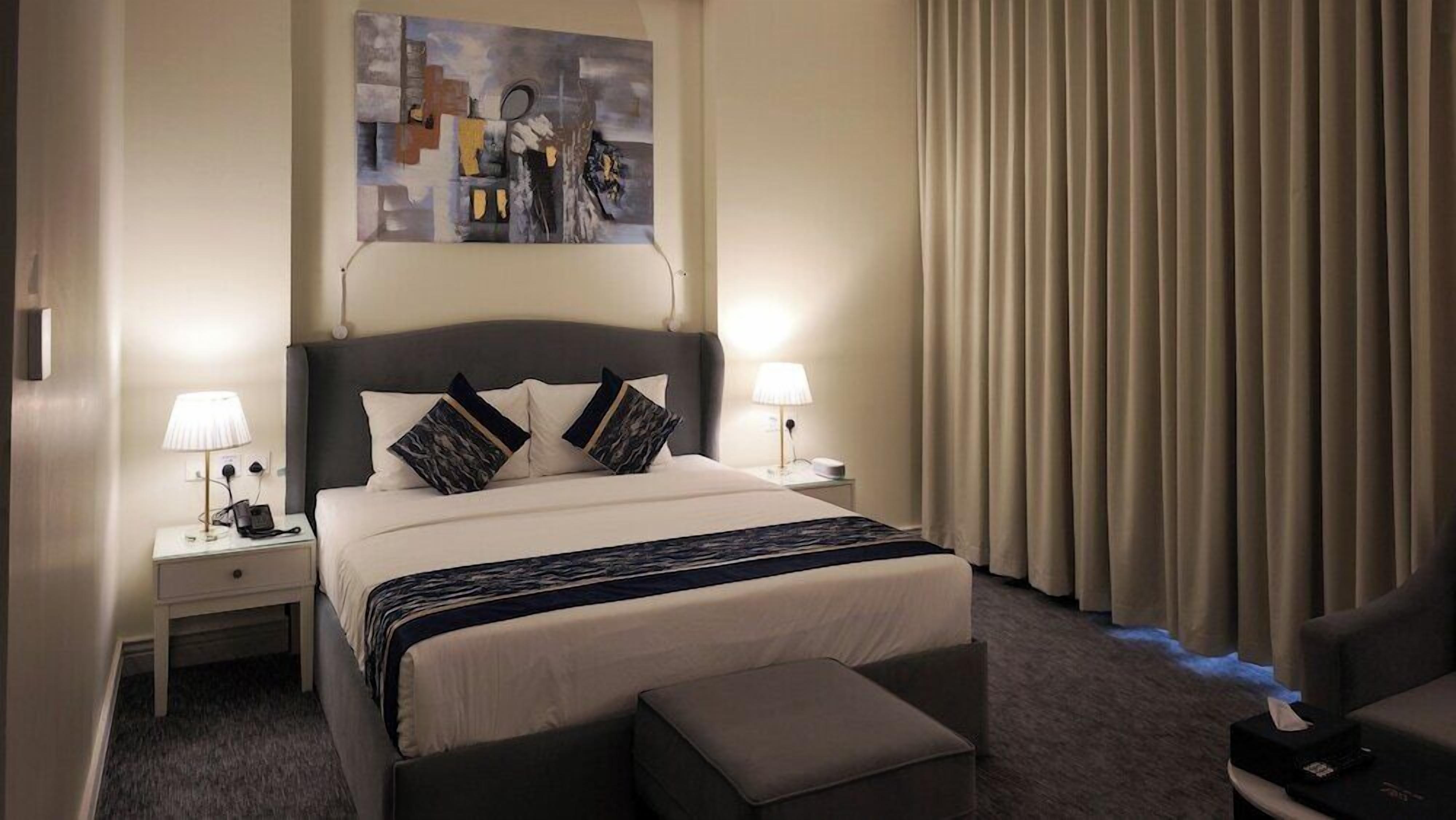 A hotel room with a bed, bedside lamps, a painting on the wall, and a curtain.