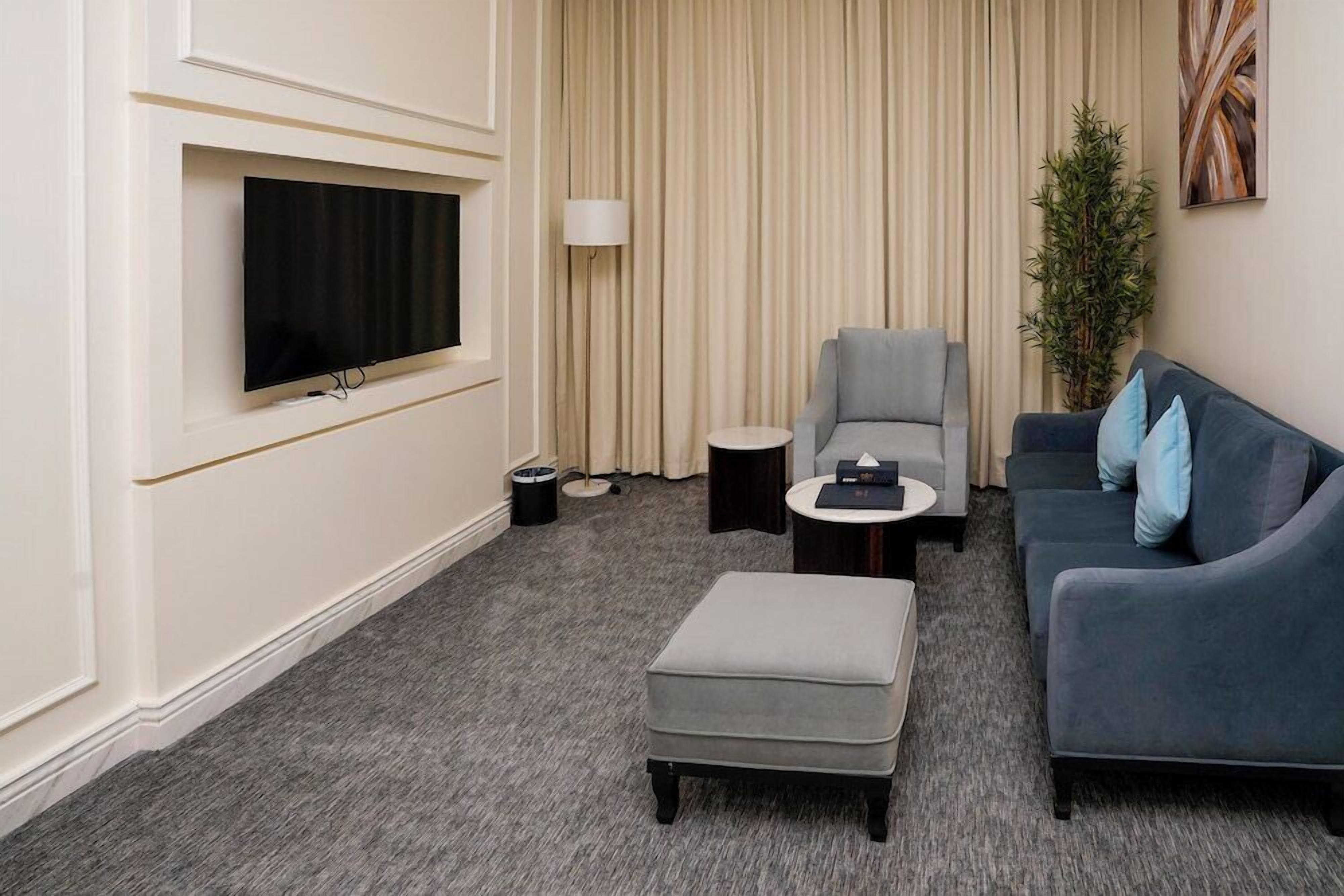 A modern living room with a flat-screen TV, grey sofa, ottoman, and a small side table.
