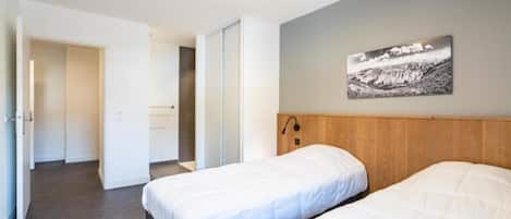 A hotel room with two beds, a wooden headboard, a wall-mounted light, and a door leading to another room.