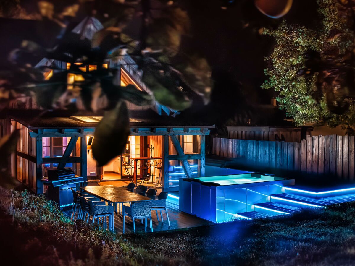 Un espace extérieur bien éclairé, comprenant une table et des chaises pour les repas, un barbecue et une piscine avec des marches illuminées.