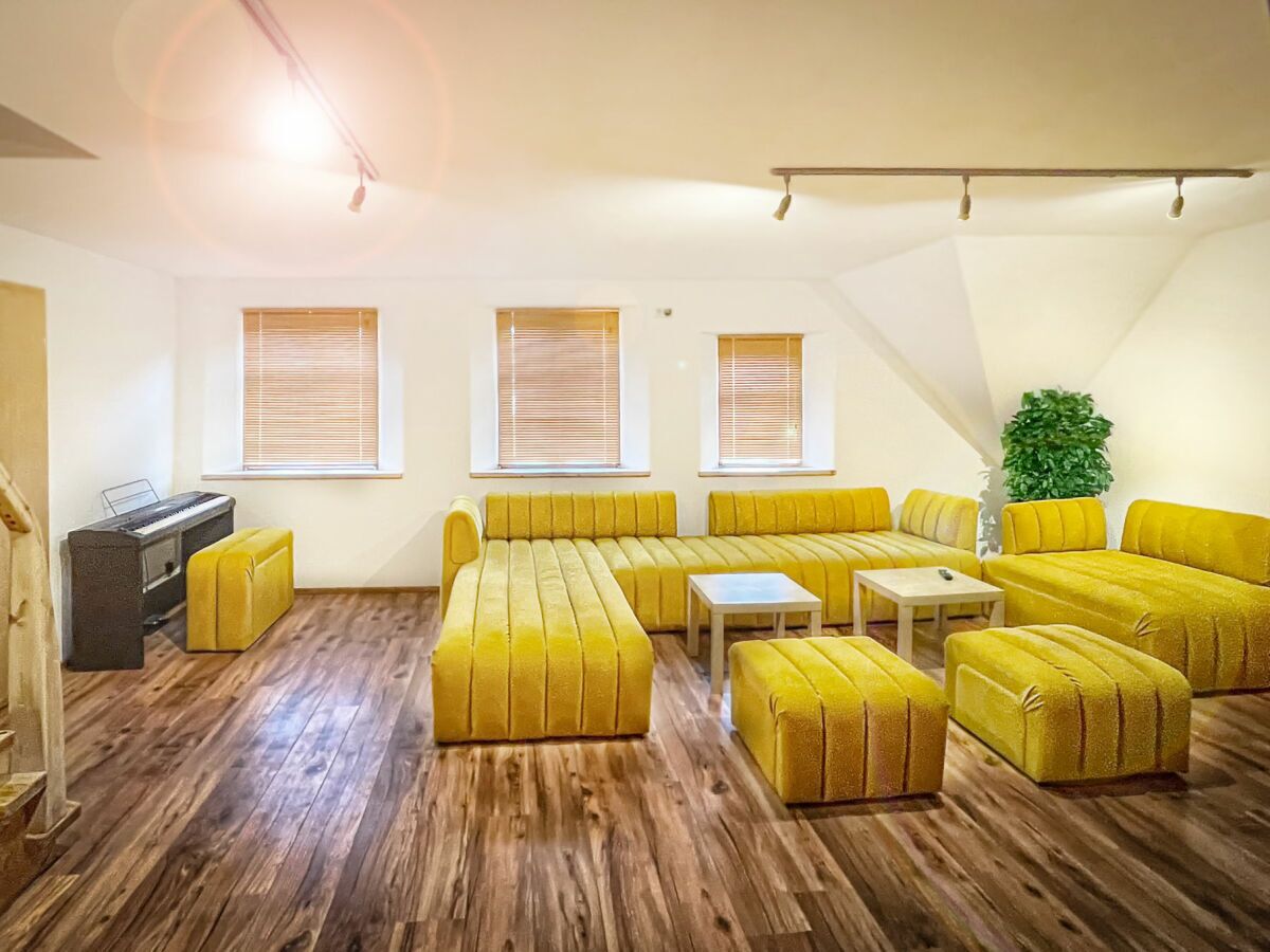 A room with a sectional sofa, a piano, and a plant.