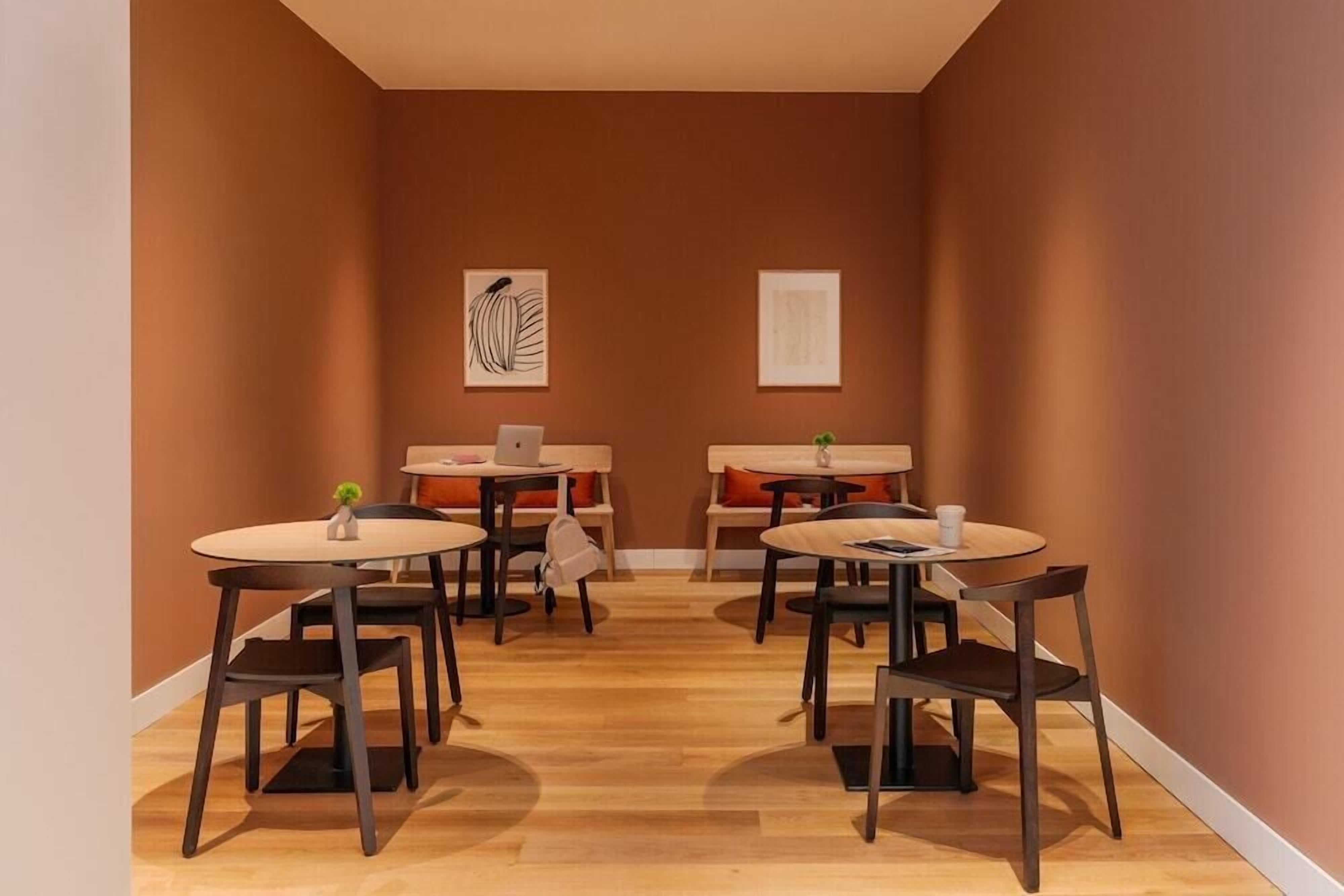 Een kamer met vier ronde tafels, elk met een stoel, en een laptop op één tafel.