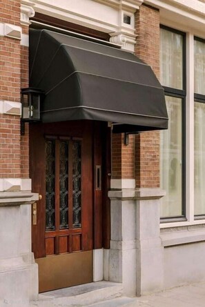 A brick building with a dark awning over a wooden door with glass panels.
