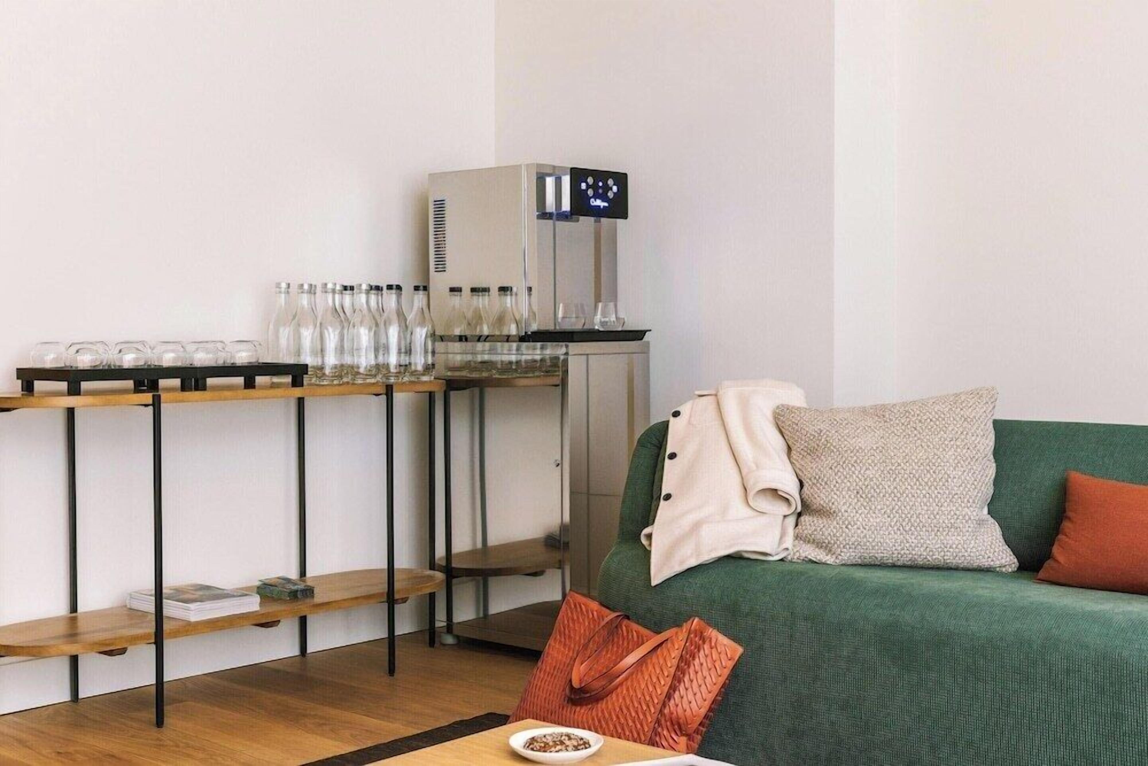 Een kamer met een groene bank, een koffieapparaat en planken met glazen flessen en glaasjes.