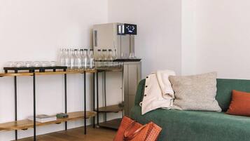 Een kamer met een groene bank, een koffieapparaat en planken met glazen flessen en glaasjes.