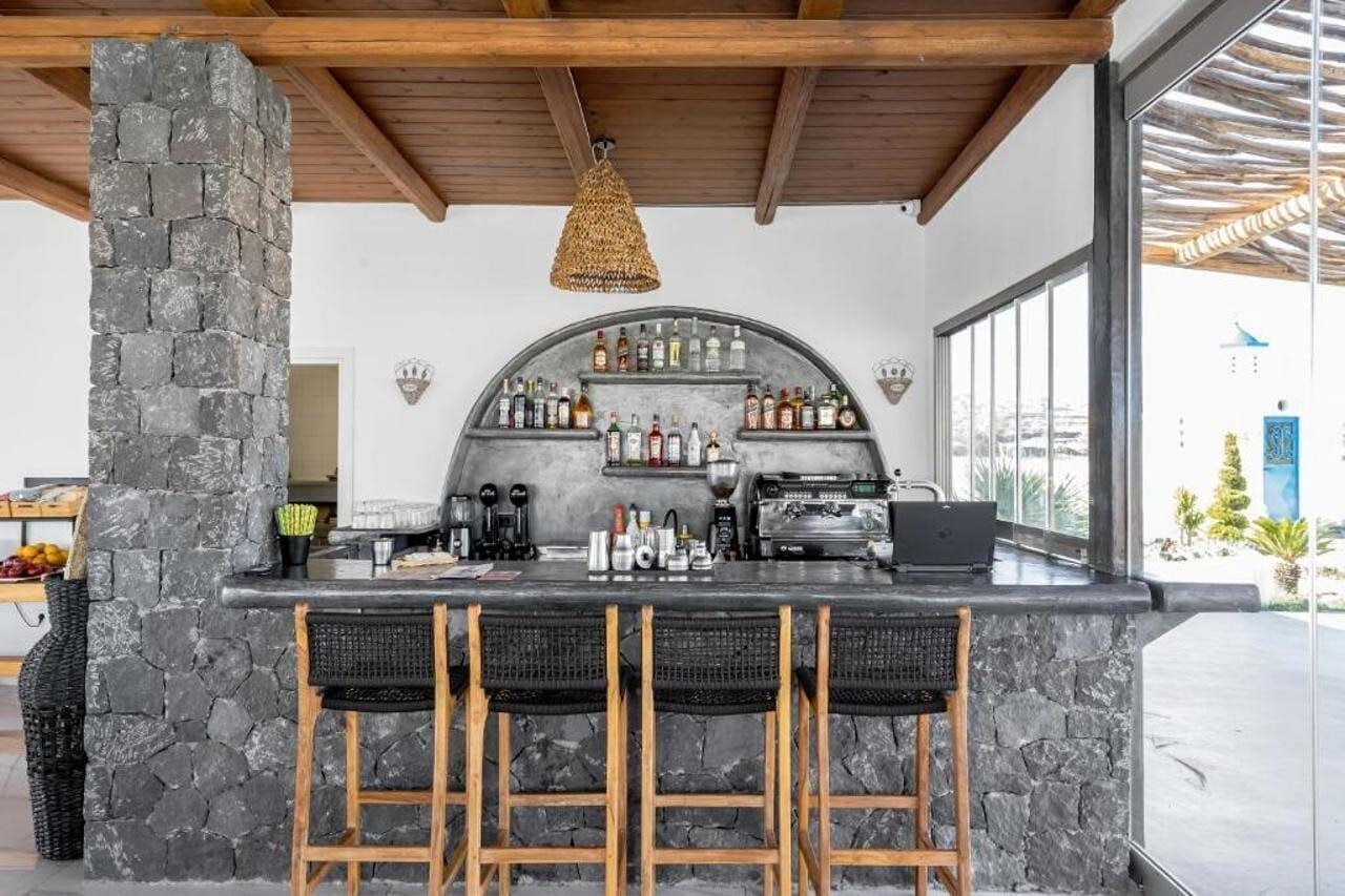A bar area with stone pillars, a curved shelving unit for bottles, and a coffee machine.