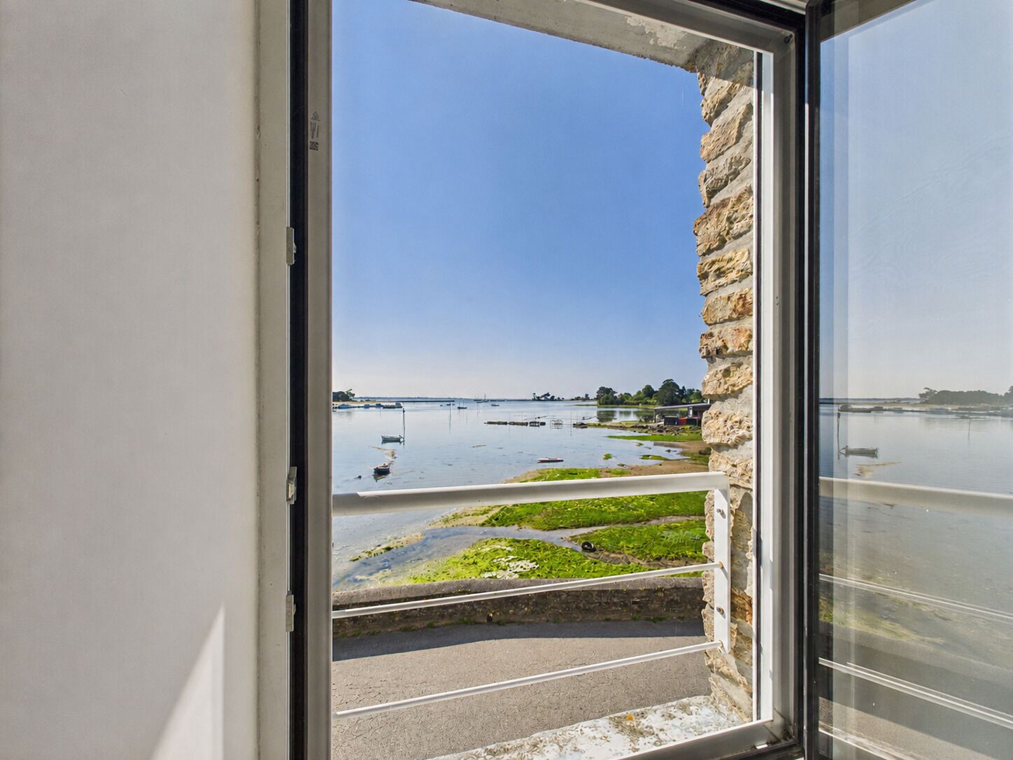 A view through a window with a stone wall, a body of water, and boats.