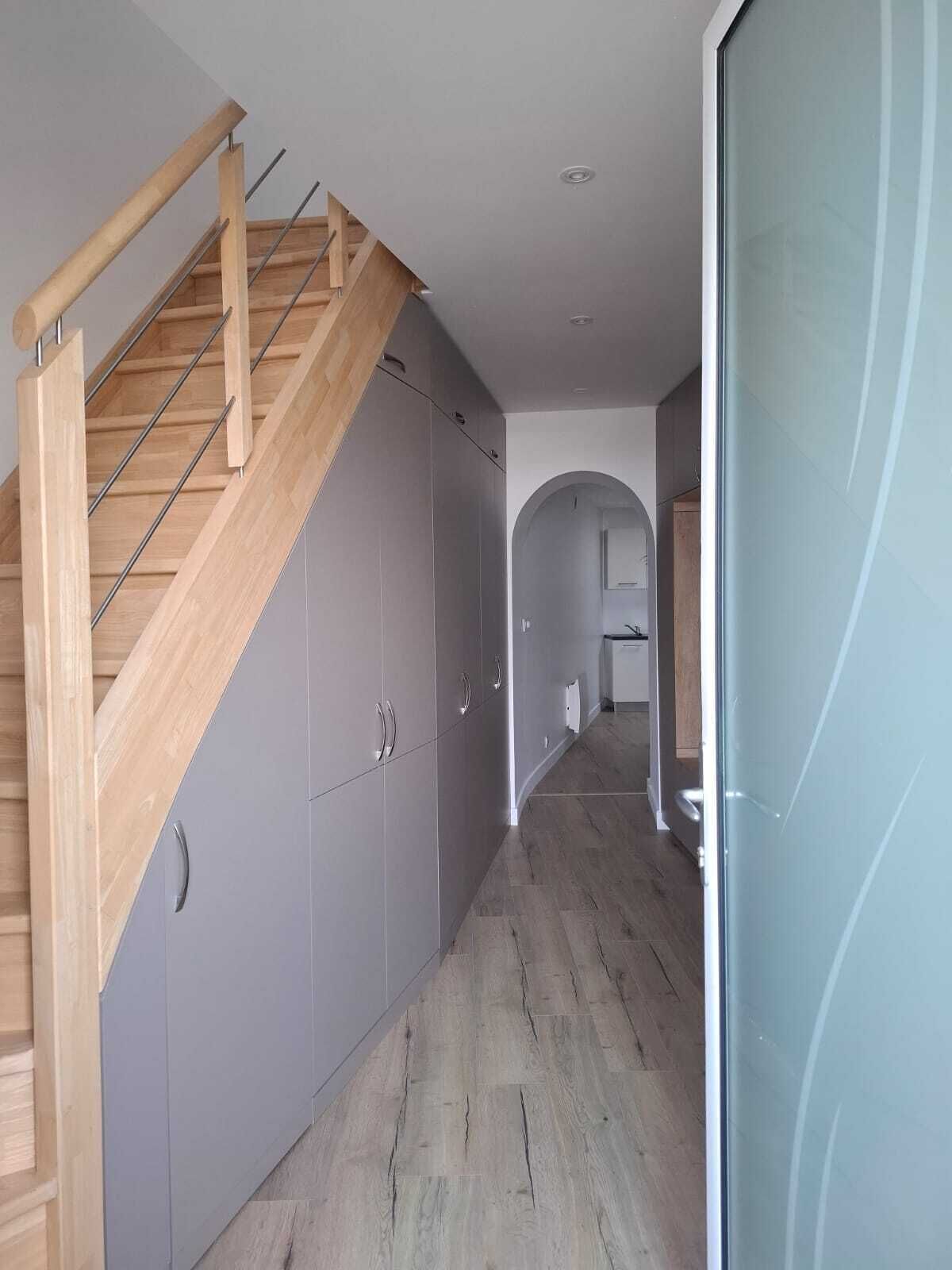A modern interior with a wooden staircase, grey cabinets, and a hallway leading to a kitchen area.