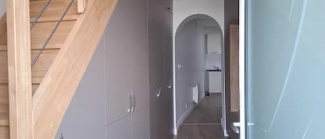 Ein modernes Interieur mit einer Holztreppe, grauen Schränken und einem Flur, der in einen Küchenbereich führt.