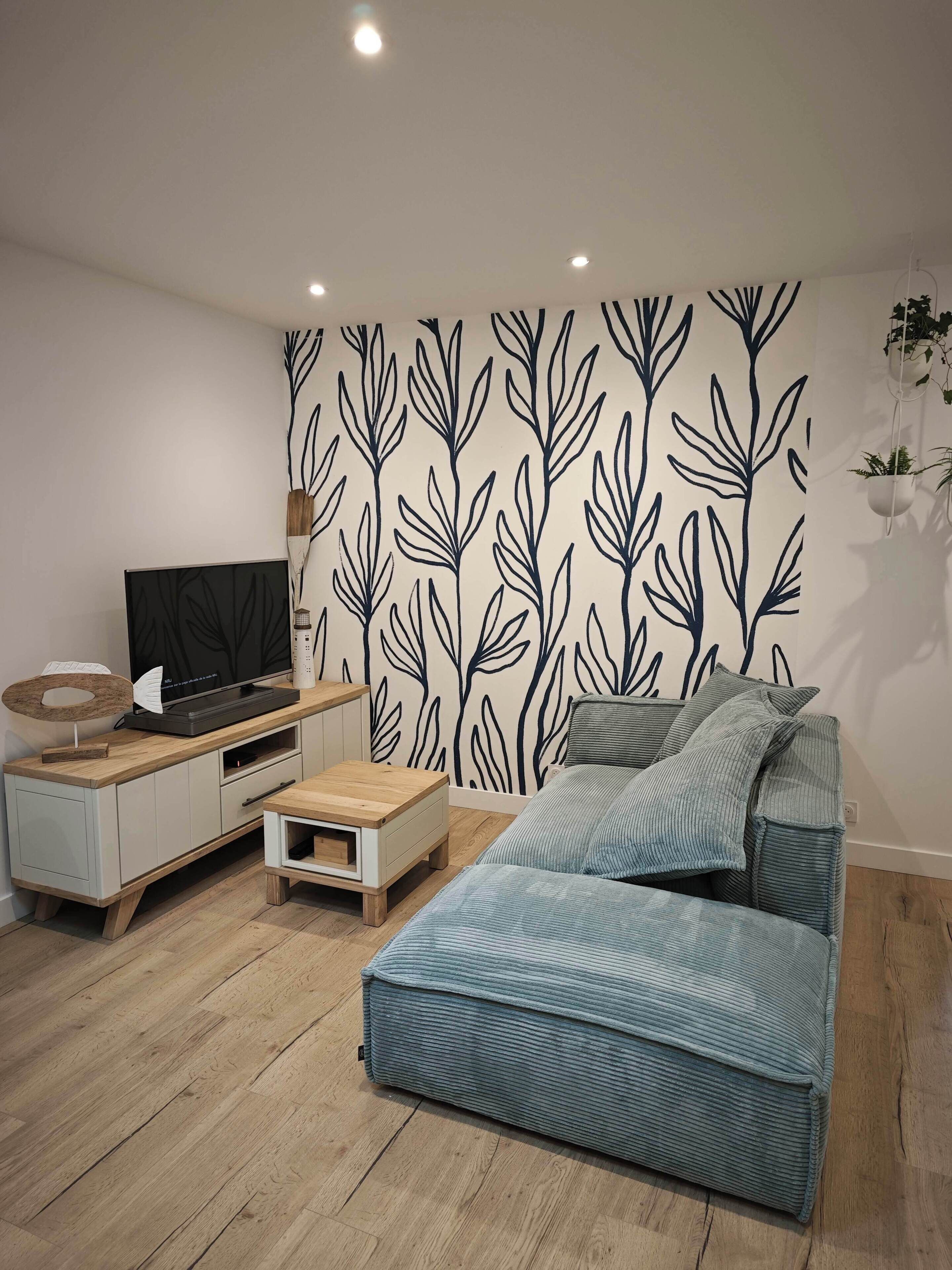 A modern living room with a flat-screen TV, a wooden coffee table, a sofa, and a wall with a leaf pattern.