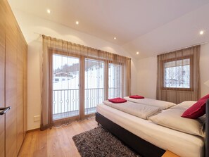 Ein Schlafzimmer mit einem großen Bett, zwei mit Vorhängen versehenen Fenstern, Holzboden und einem Balkon mit Geländer.