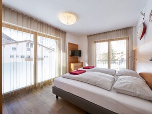 A hotel room with a bed, a TV mounted on the wall, and large windows with curtains. - Apartments Grischuna Mountain Lodge, (Samnaun-Dorf) by Interhome (Samnaun)