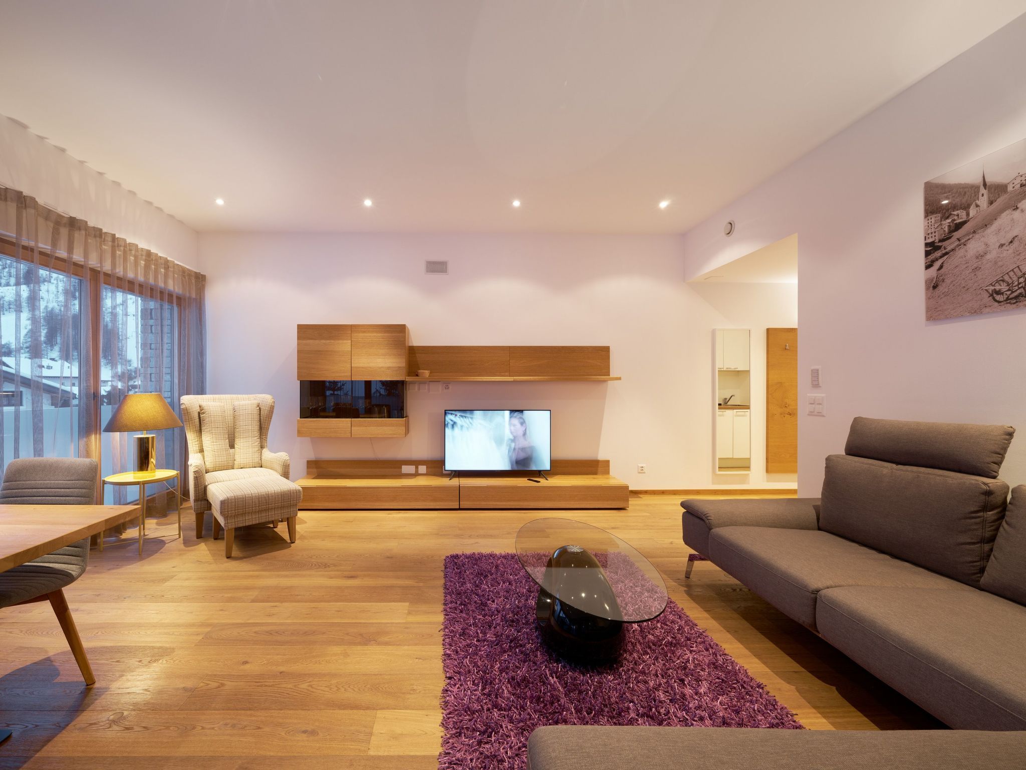 A modern living room with a sofa, armchair, TV, and wooden flooring.