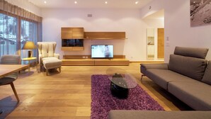 Ein modernes Wohnzimmer mit Holzboden, einer Couch, einem Sessel, einem Fernseher und einem großen Fenster.