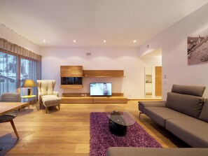 A modern living room with a wooden floor, a sofa, a chair, a TV, and a large window. - Apartments Grischuna Mountain Lodge, (Samnaun-Dorf) by Interhome (Samnaun)