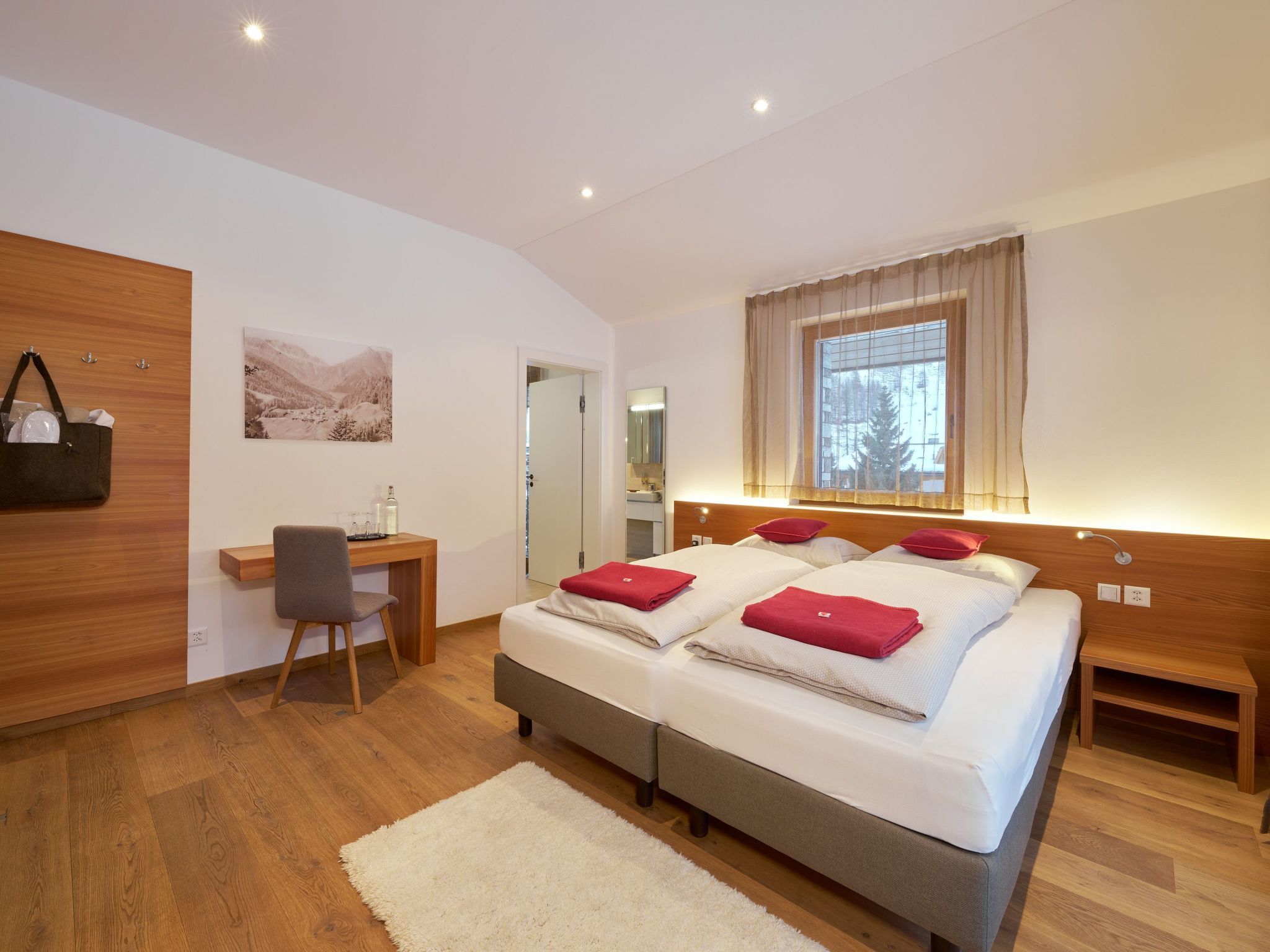 A modern hotel room with a double bed, a desk, a chair, and a large window.