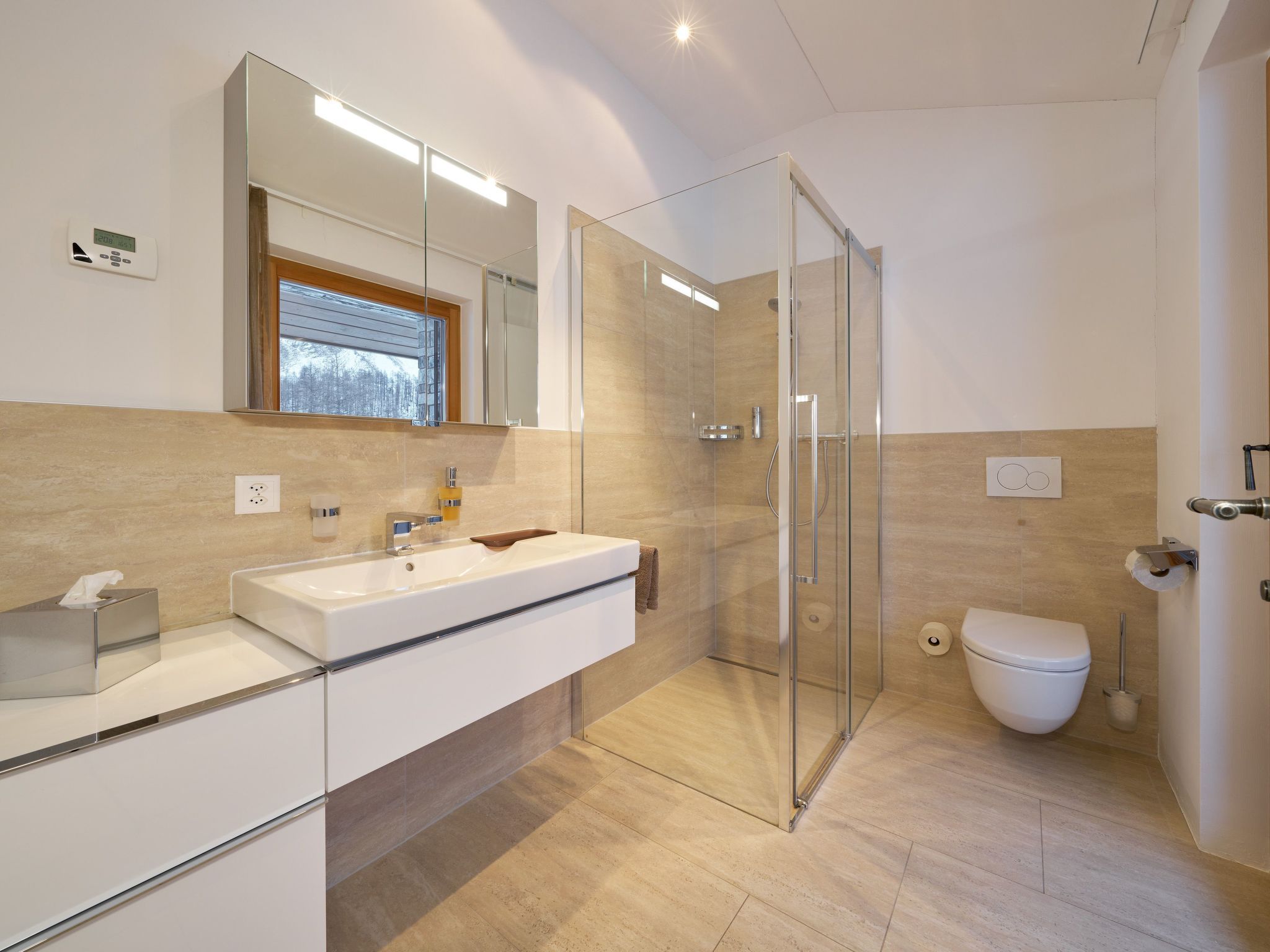 Et moderne badeværelse med en glasafskærmet brusekabine, en hvid vask og et toilet.