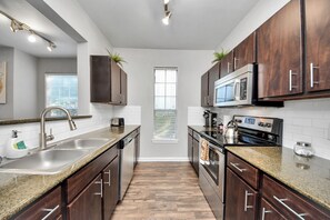 A modern kitchen with dark wood cabinets, stainless steel appliances, a granite countertop, and a window with blinds. - 2Bedrooms 3 Beds apartment in soothing Med Center Houston with Pool and Gym (Houston)