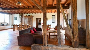 Een ruime kamer met een hoog houten plafond, een eethoek met houten meubels, en een groot raam.