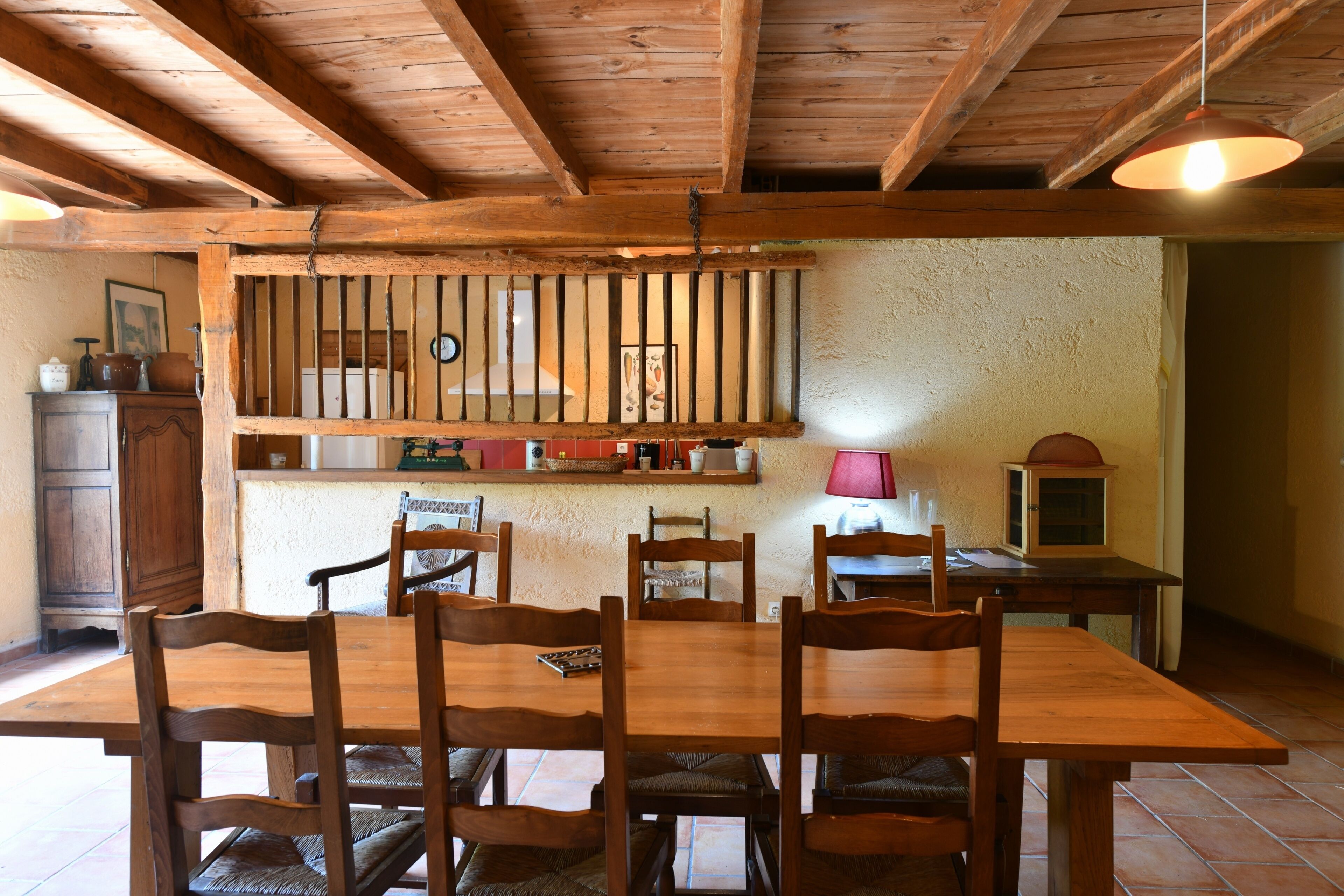A wooden dining table with six chairs, a hanging light fixture, and a rustic wall with a shelf above.