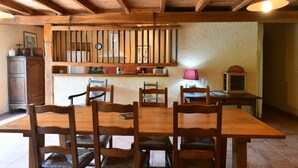 Een houten eettafel met zes stoelen, een hanglamp en een rustieke muur met een plank erboven.