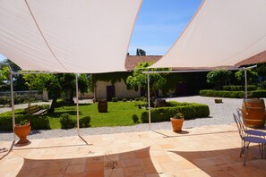 Ein Innenhof mit einer Pergola, Kübelpflanzen, einem Fass und einer gefliesten Terrasse.