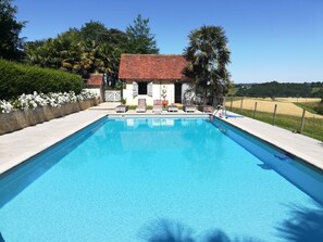 A rectangular swimming pool with a tiled deck, surrounded by a fence, and a building with a red-tiled roof in the background. - Charming estate for 14 people with a pool, lake, and private grounds (Arrosès)