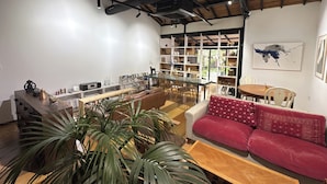 A spacious living area with a high ceiling, a dining table, a red sofa, and a bookshelf filled with various items. - Machiya Coliberty | Private Villa for 8 | 10 minutes to Kinkaku-ji and Nijo Castle (京都市上京区竪社北半町)