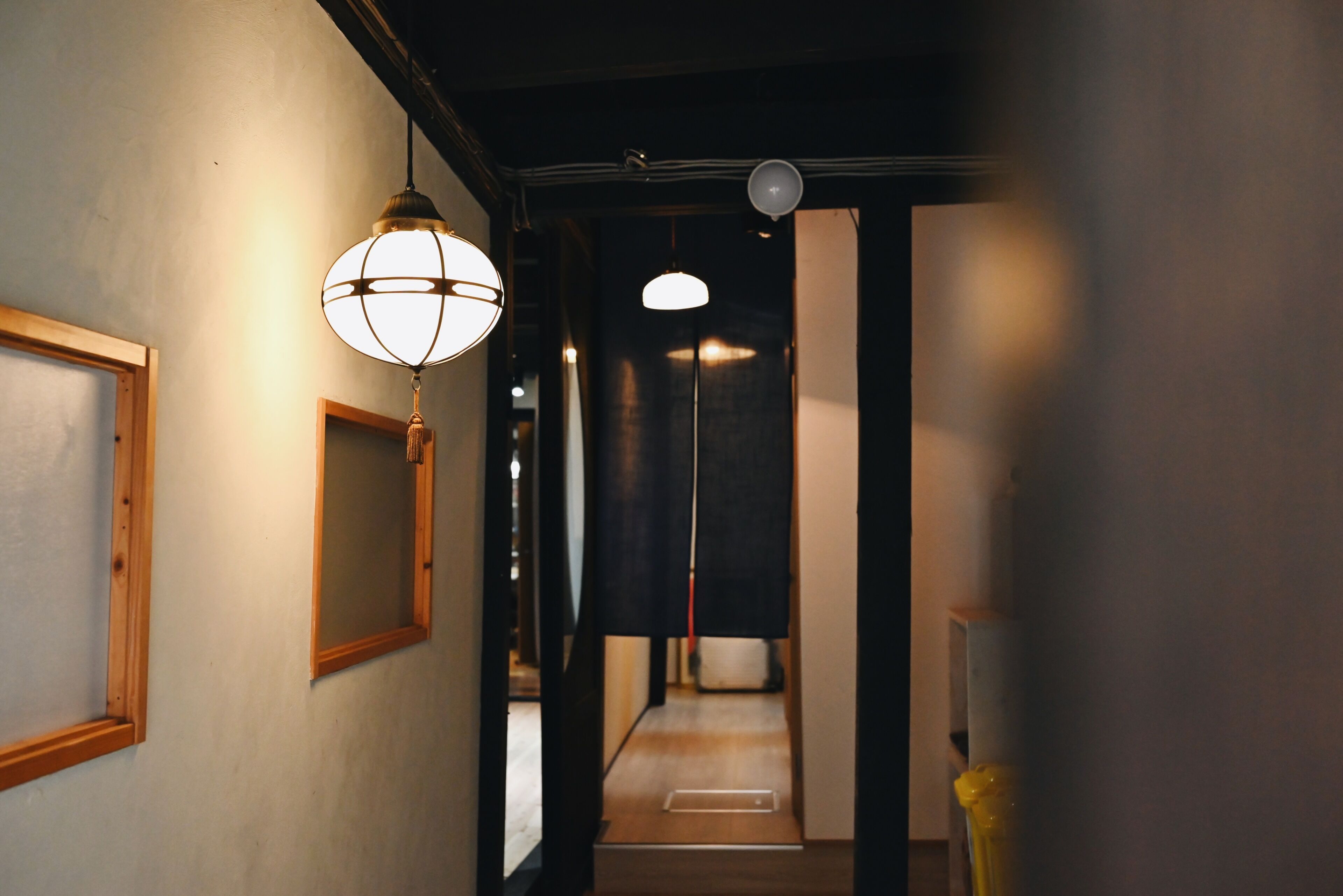 A hallway with a wooden-framed mirror, a hanging globe light, and a ceiling-mounted light fixture.