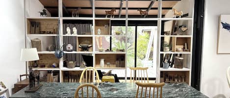 Un comedor con una mesa de mármol, dos sillas de madera y una estantería de madera llena de diversos objetos.