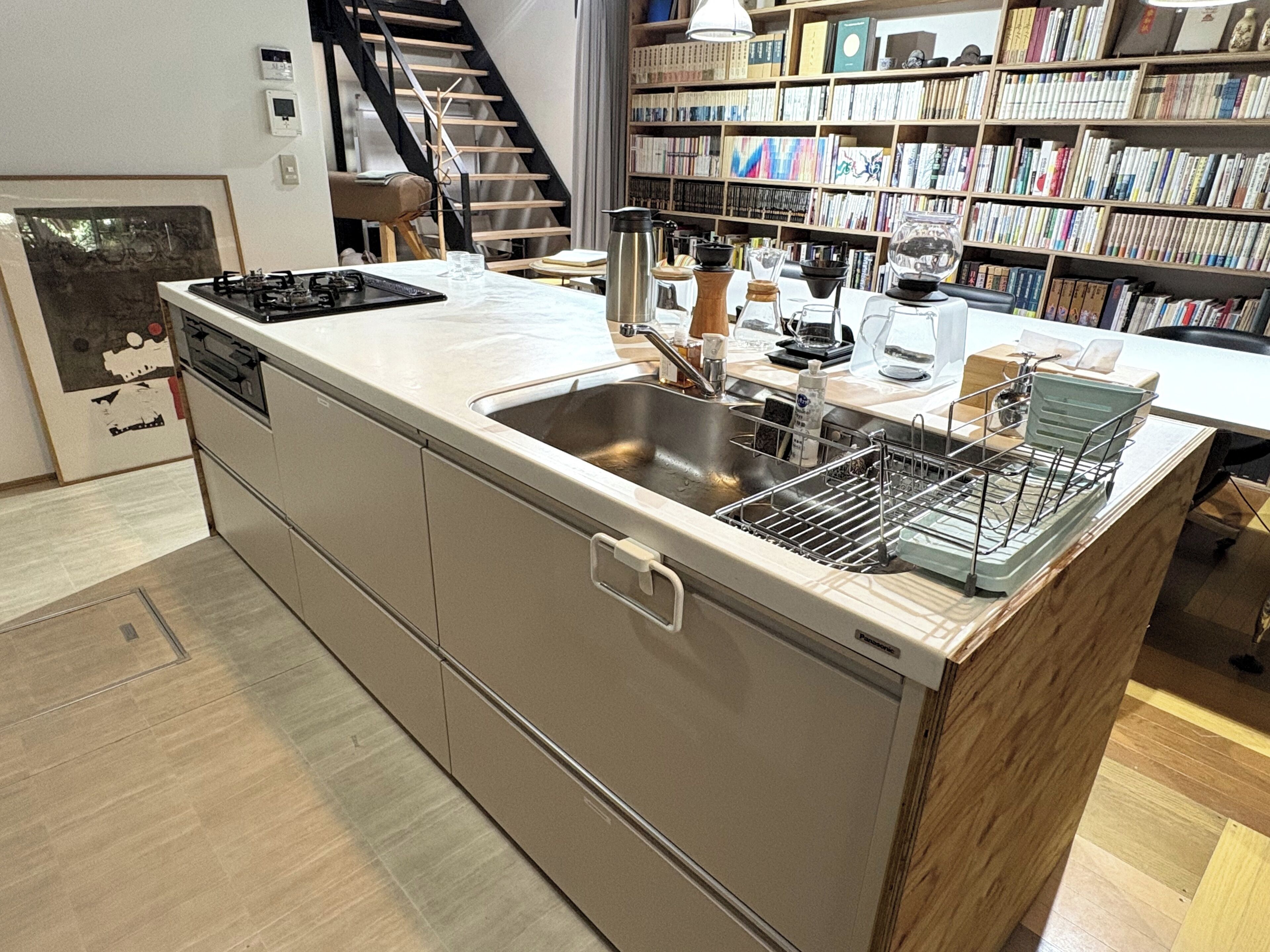A modern kitchen with a built-in dishwasher, a sink, and a stove. There is a bookshelf filled with books in the background.