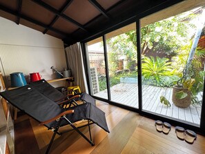 Ein Zimmer mit einer großen Schiebeglasdoor zum hölzernen Deck, einem schwarzen Klapptisch und einem Paar Hausschuhen auf dem Boden.