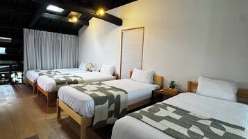 A hotel room with three beds, wooden headboards, a large window with curtains, and a ceiling with exposed beams and lighting.