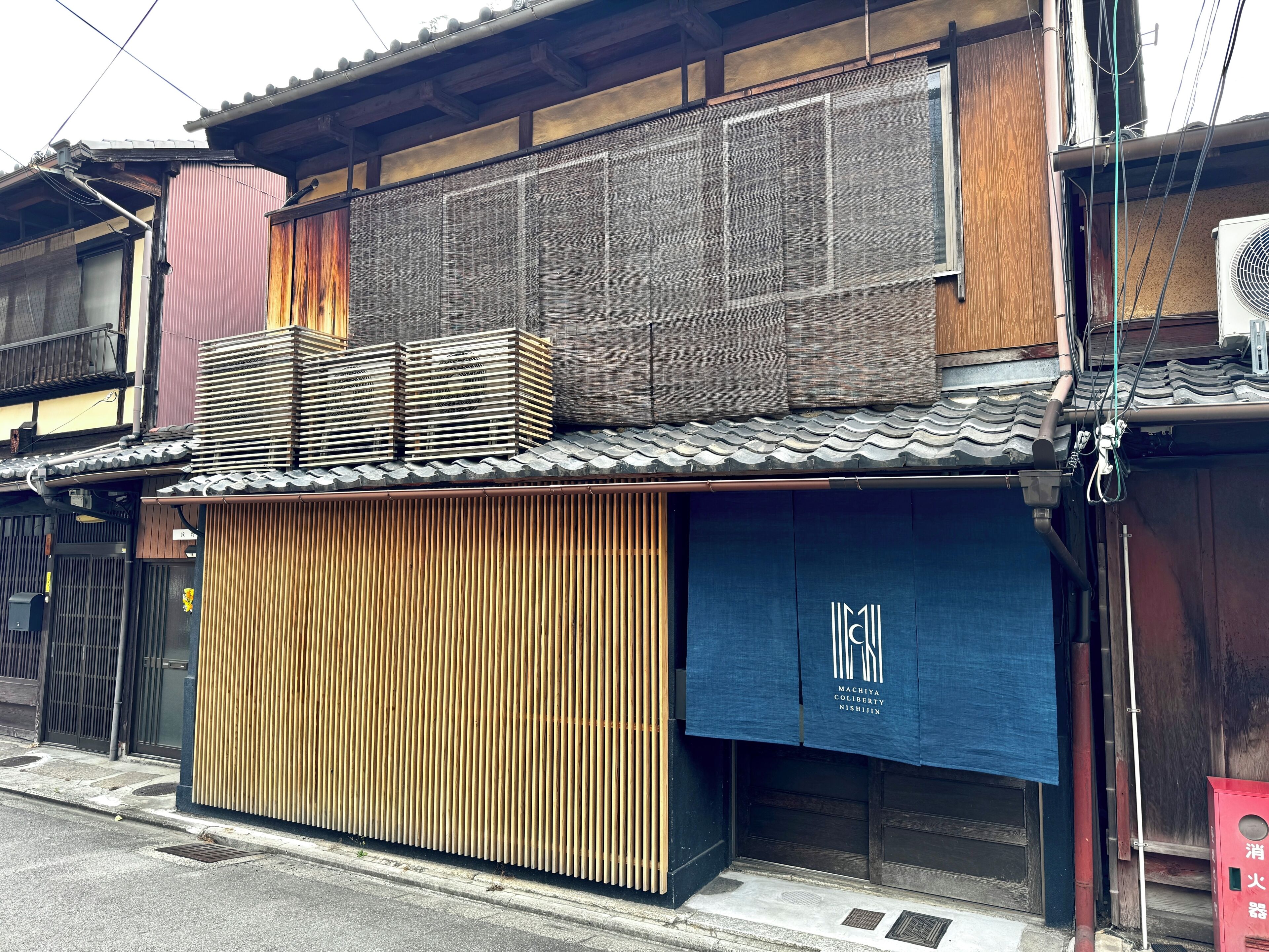 A traditional Japanese building with a wooden facade, a tiled roof, and a blue awning with white text.