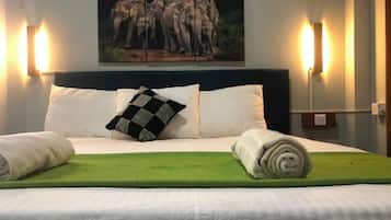 A hotel room with a bed, pillows, a green throw, and a painting of elephants on the wall.
